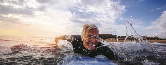Active and happy senior man living to the fullest, surfing on a surfboard during his summer vacation