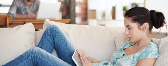 Shot of an attractive young woman using her digital tablet while reclining on the sofa at home