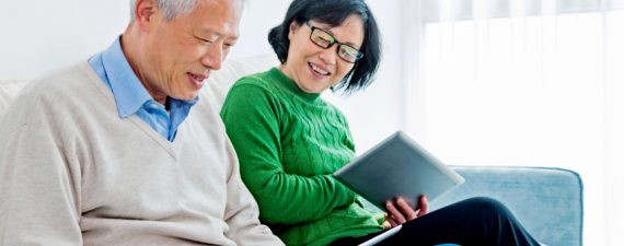 Happy senior asian couple sitting on sofa and reading on a digital tablet at home.