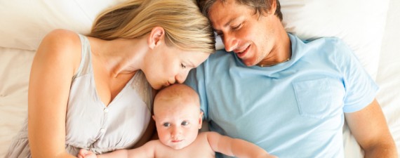 Caring parents with baby lying in bed. Horizontal Shot.